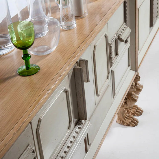 Aparador de madera Lamassu con puertas decoradas y patas talladas en un salón luminoso