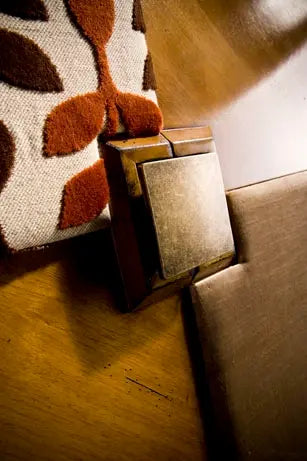 Detalle de tirador cuadrado del Armario Dinastía sobre paneles de madera y tejido con motivos en tonos rojizos.