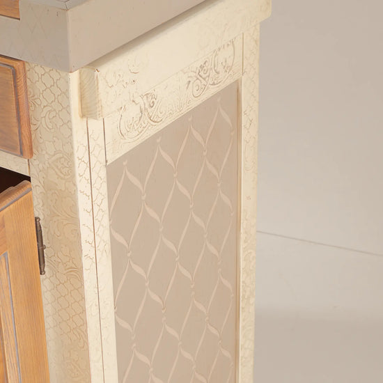 Detalle lateral del Banco Kitchen con acabado crema, motivos decorativos y puerta de madera.