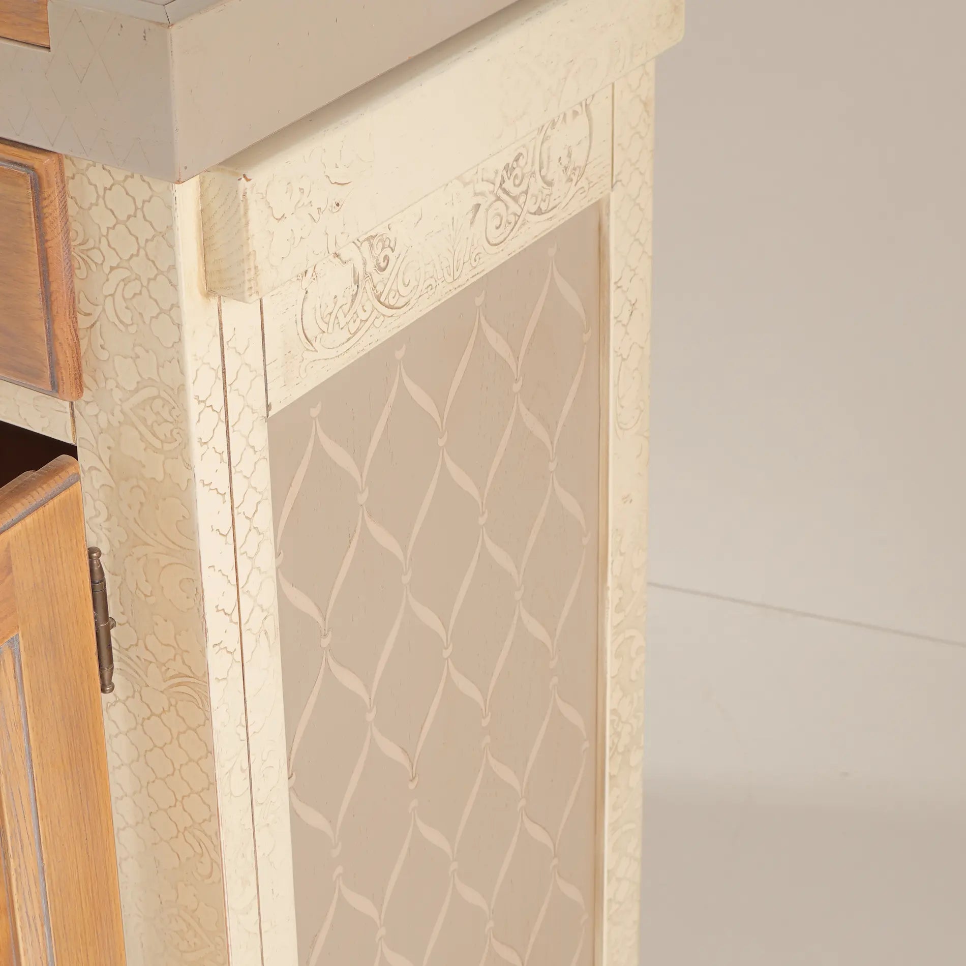 Detalle lateral del Banco Kitchen con acabado crema, motivos decorativos y puerta de madera.