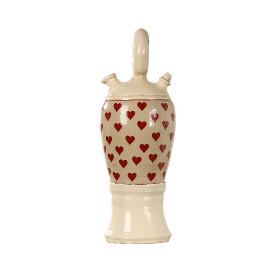 Botijo Love de cerámica esmaltada con corazones rojos, acabado crema, asa circular superior y base elevada sobre fondo blanco.