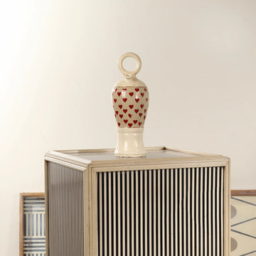 Botijo Love de cerámica con corazones rojos colocado sobre un mueble decorativo de rayas en un ambiente interior.