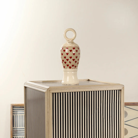 Botijo Love de cerámica con corazones rojos colocado sobre un mueble decorativo de rayas en un ambiente interior.