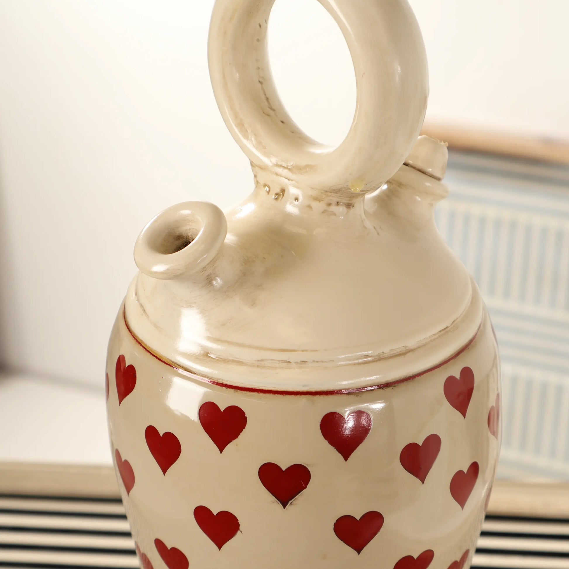 Detalle del asa circular y la boca del Botijo Love de cerámica esmaltada en tono crema con corazones rojos.