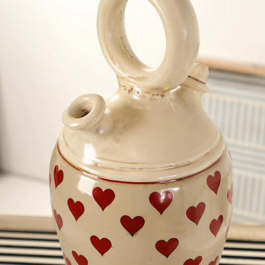 Detalle del asa circular y la boca del Botijo Love de cerámica esmaltada en tono crema con corazones rojos.
