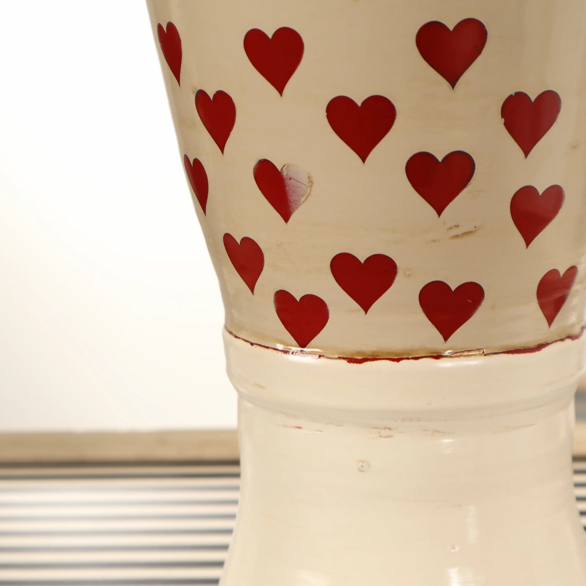 Detalle del cuerpo del Botijo Love con corazones rojos sobre cerámica esmaltada en tono crema y base elevada.