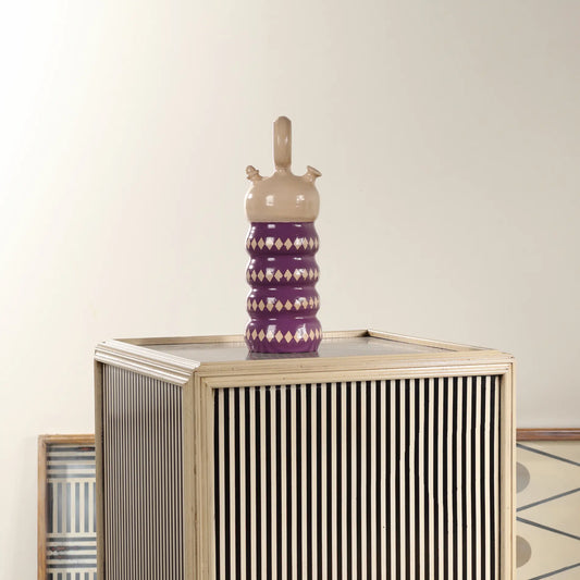 Botijo Rombos de cerámica morada colocado sobre un mueble decorativo de rayas en un ambiente interior.