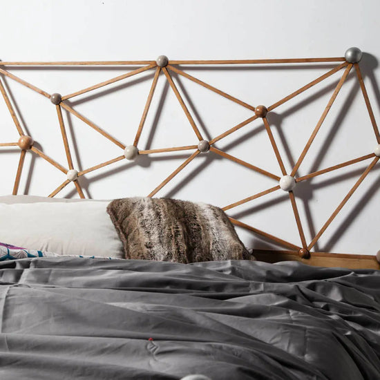 Cama Átomos con cabecero geométrico artesanal en madera maciza y composición inspirada en estructuras moleculares.