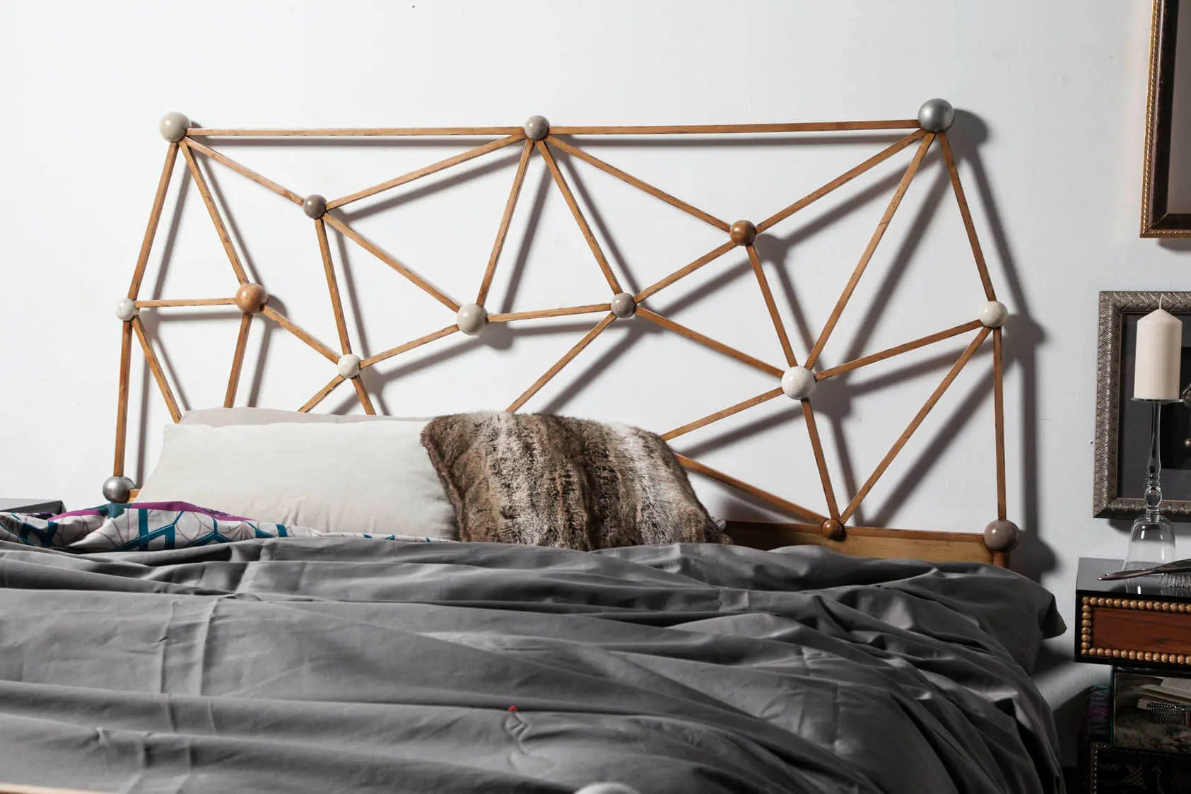 Cama Átomos con cabecero geométrico artesanal en madera maciza y composición inspirada en estructuras moleculares.