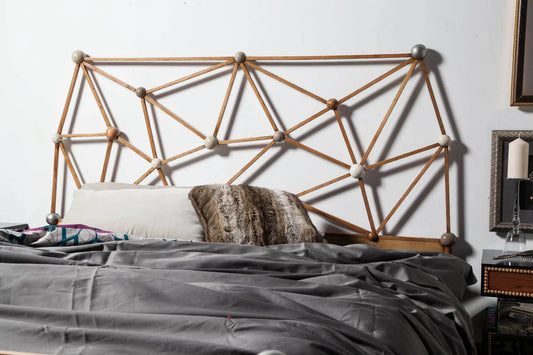 Cama Átomos con cabecero geométrico artesanal en madera maciza y composición inspirada en estructuras moleculares.