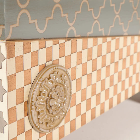 Detalle de la Casita Divina con damero en tonos naturales y rosetón ornamental en relieve.