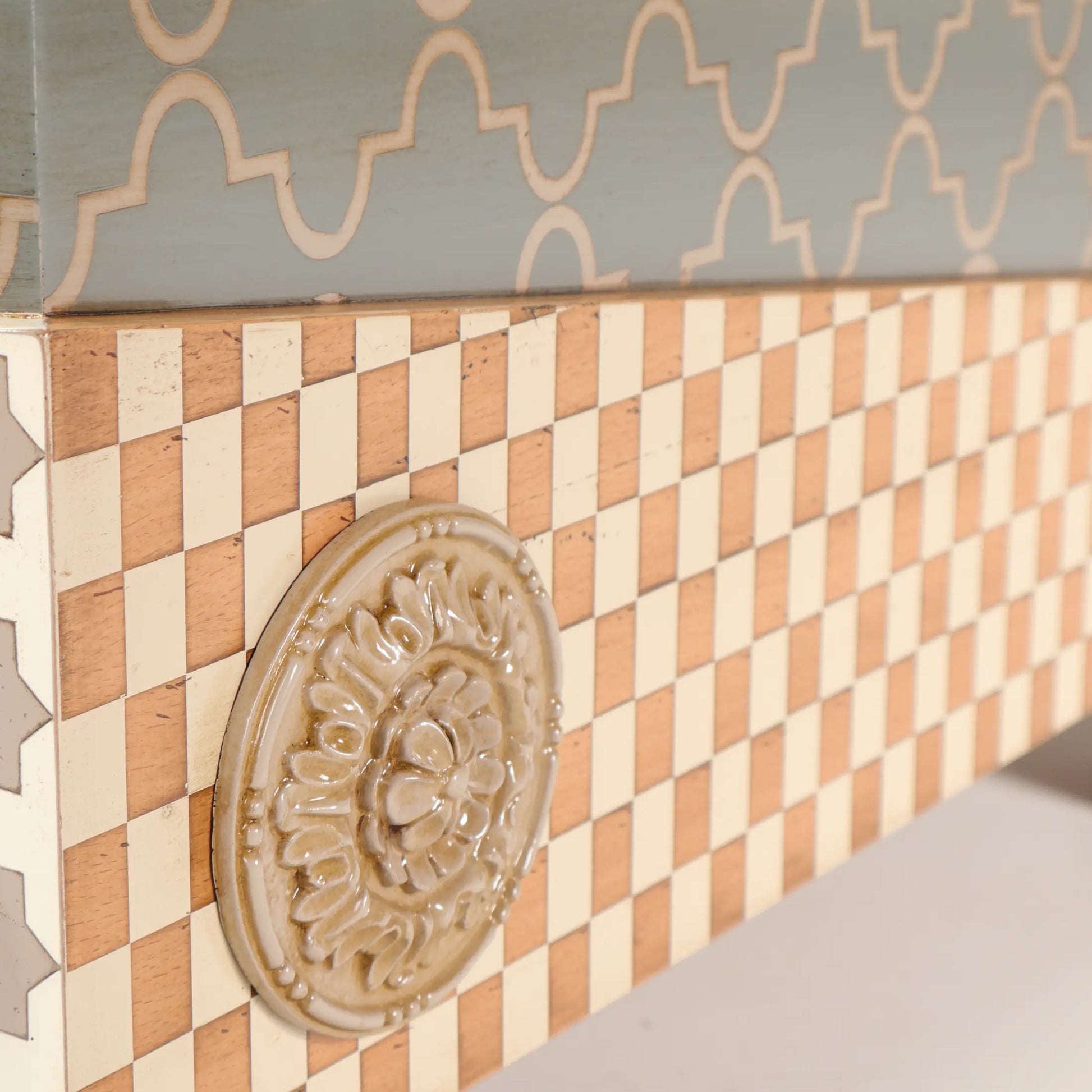 Detalle de la Casita Divina con damero en tonos naturales y rosetón ornamental en relieve.