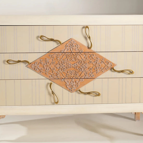 Detalle frontal de la cómoda Cait con motivo ornamental y tiradores escultóricos.