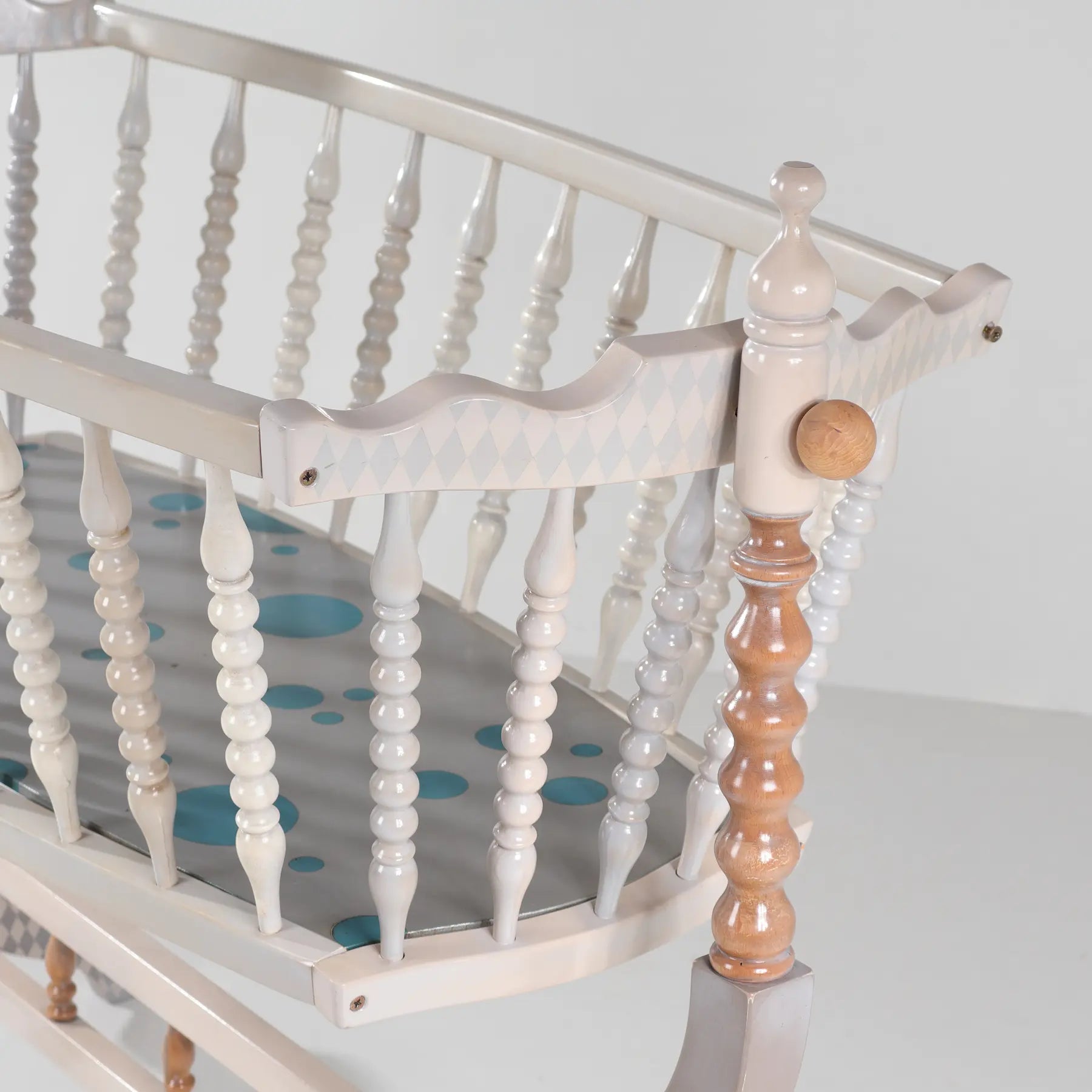 Barandilla torneada blanca de la cuna Bambino con detalles en madera natural.