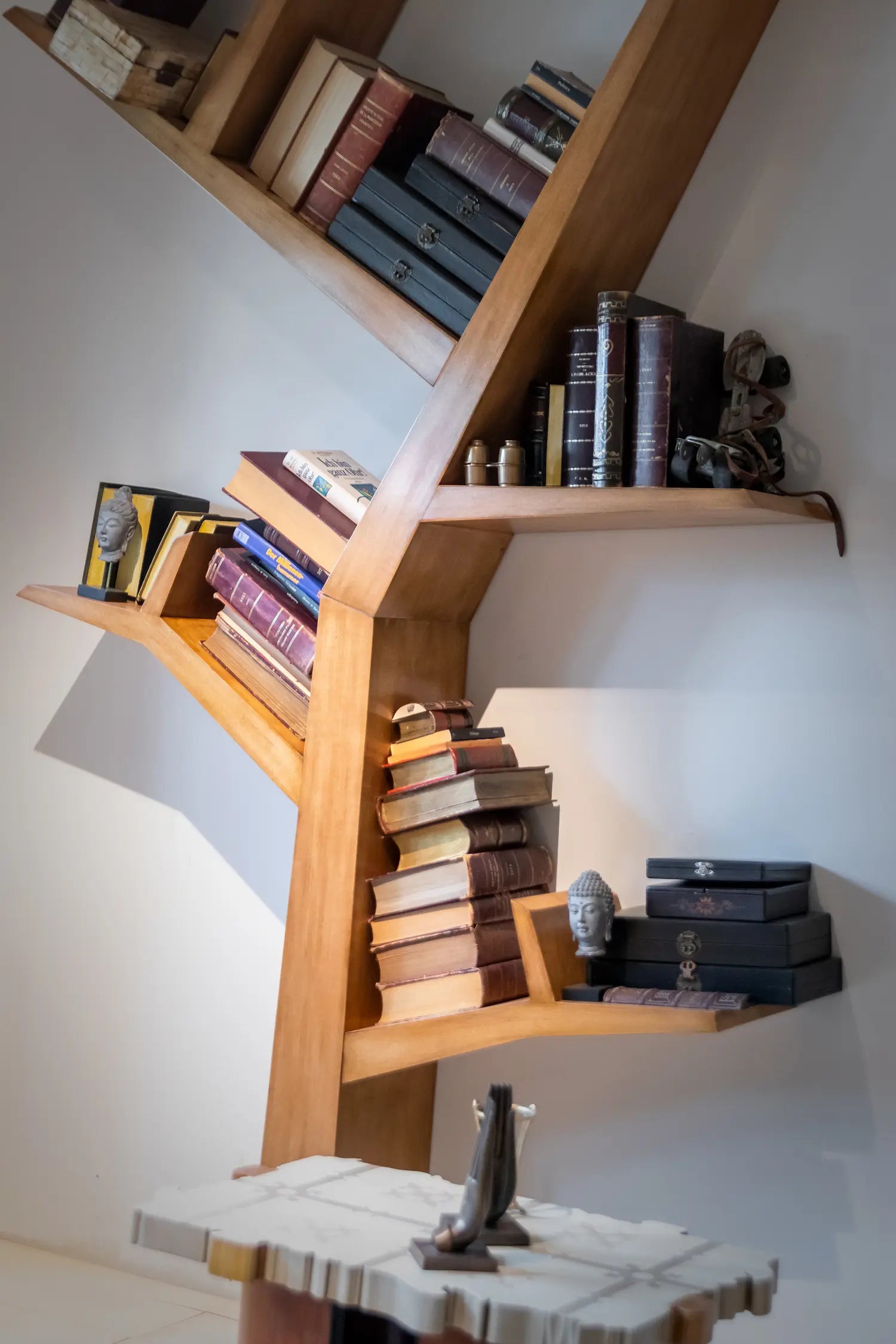 Detalle de las baldas inclinadas del librero Tree vertical con libros y objetos decorativos.