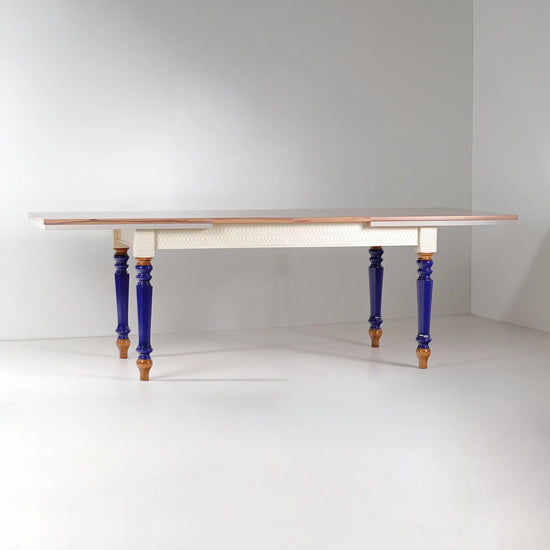 Mesa de comedor extensible Cascabella con sobre geométrico, faldón blanco y patas azul cobalto.