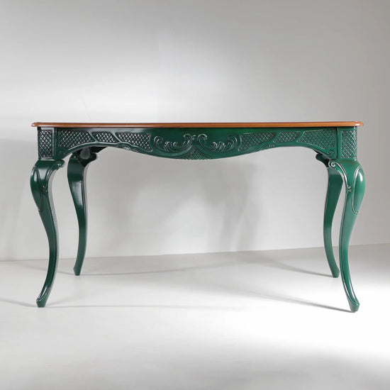 Vista frontal de la mesa de comedor Dafoe con faldón ornamental en verde profundo.