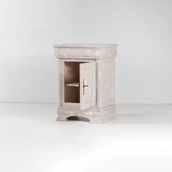 Mesilla de noche Giuletta con puerta abierta y acabado claro con lunares decorativos.