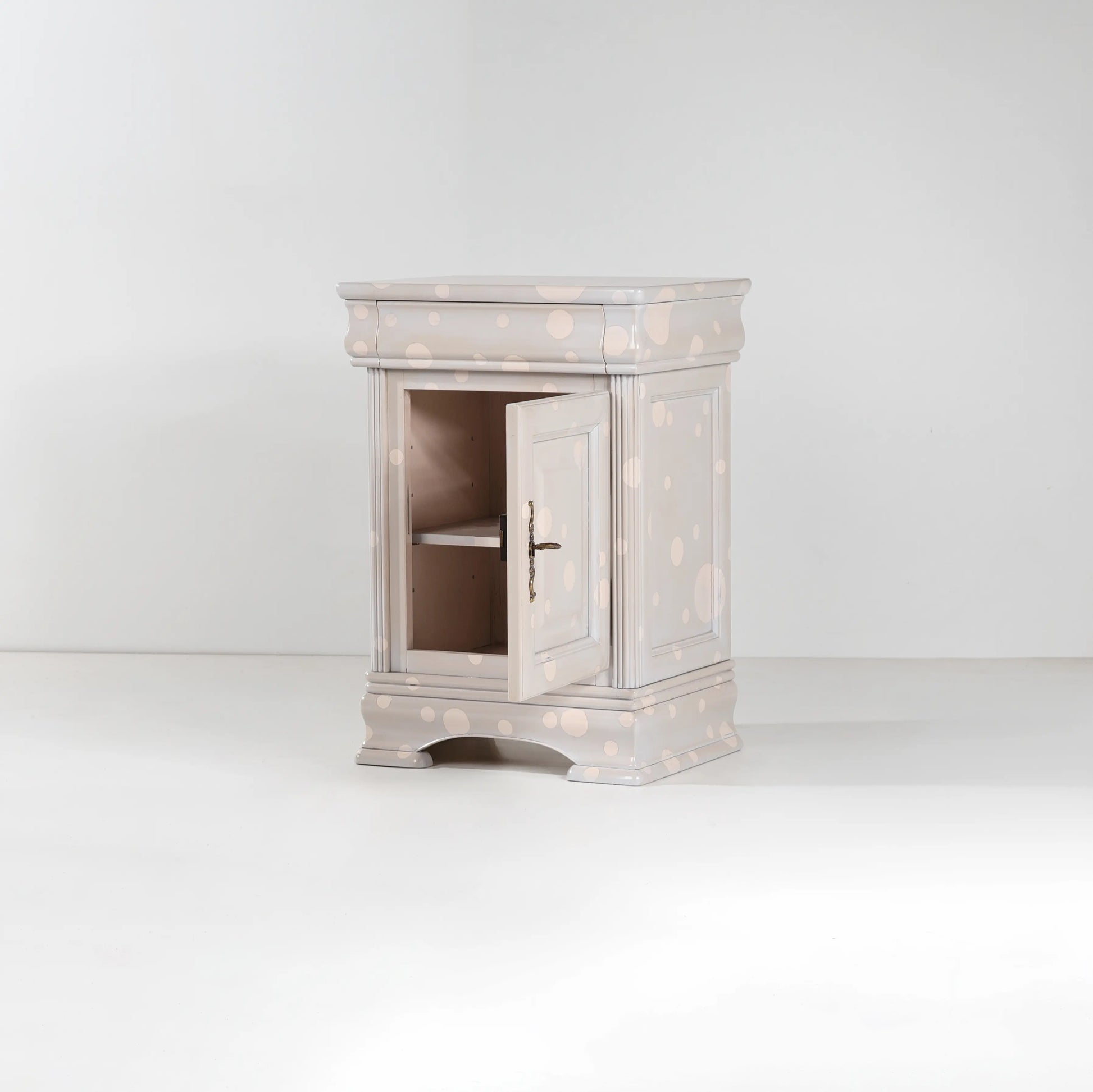 Mesilla de noche Giuletta con puerta abierta y acabado claro con lunares decorativos.