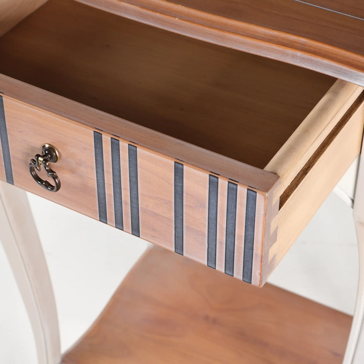 Cajón abierto de la mesita Fini con tirador de anilla y franjas decorativas oscuras.