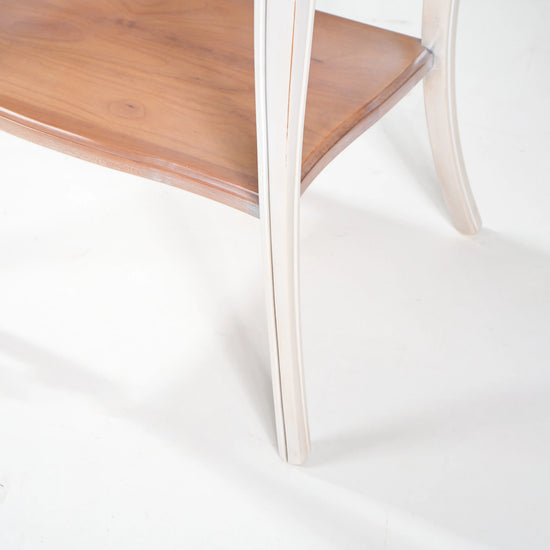Mesita Fini en tonos marfil y madera con cajón decorado, patas curvas y estante inferior.