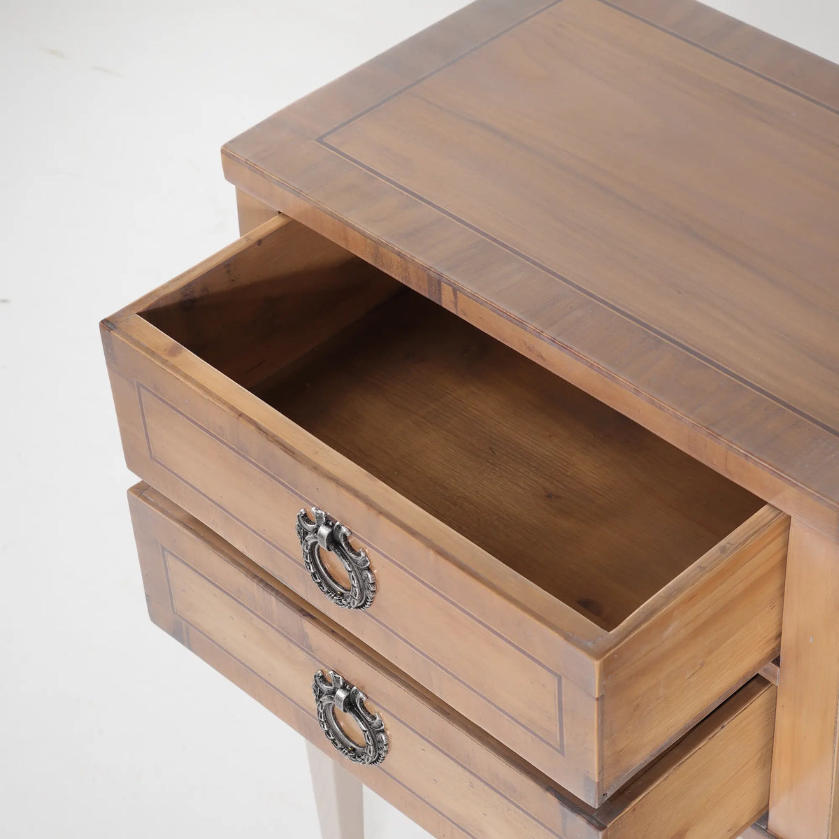 Mesita de noche Chely con cajón abierto, acabado en tonos madera y tiradores ornamentales.