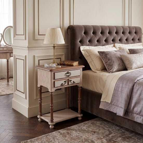 Mesita de noche Nimes junto a la cama en un dormitorio elegante de inspiración clásica.