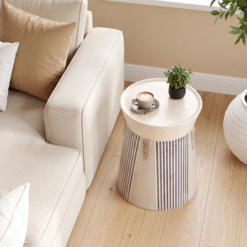 Mesita Tambor junto al sofá, como mesa lateral de salón con diseño decorativo en tonos claros.