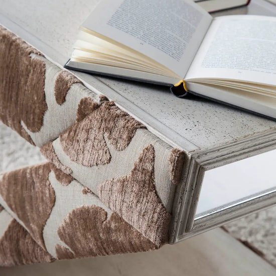 Detalle de la Mesita Z con acabado textil en tonos tierra, superficie envejecida y libro abierto sobre la mesa auxiliar de diseño.