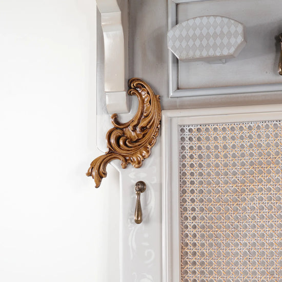 Detalle del aplique ornamental del Perchero Rejilla con acabado cálido y estructura en tono claro.