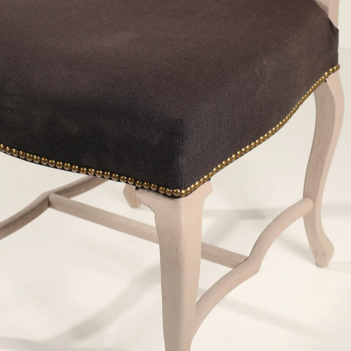Detalle del asiento tapizado de la Silla Cluster con tachuelas y patas curvas claras.