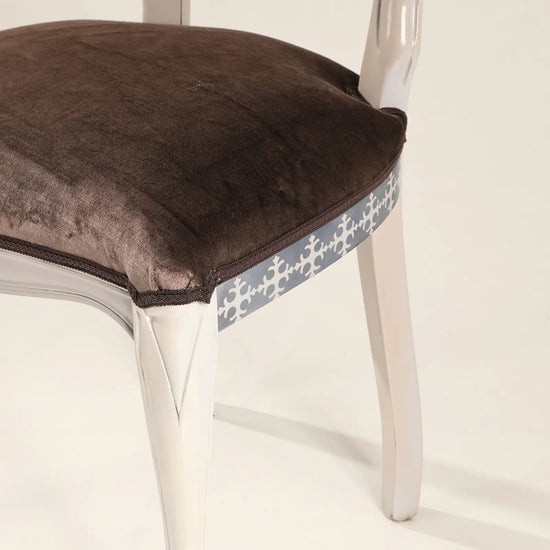 Detalle del asiento tapizado marrón de la Silla Manila con cenefa decorativa.
