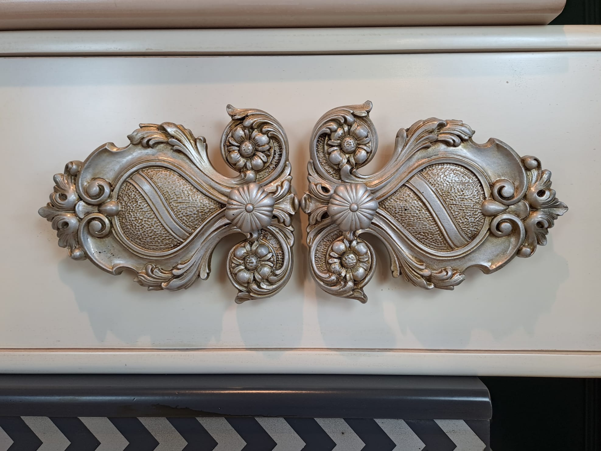 Detalle del Sinfonier Alice con gran aplique central de estilo barroco en acabado metálico.