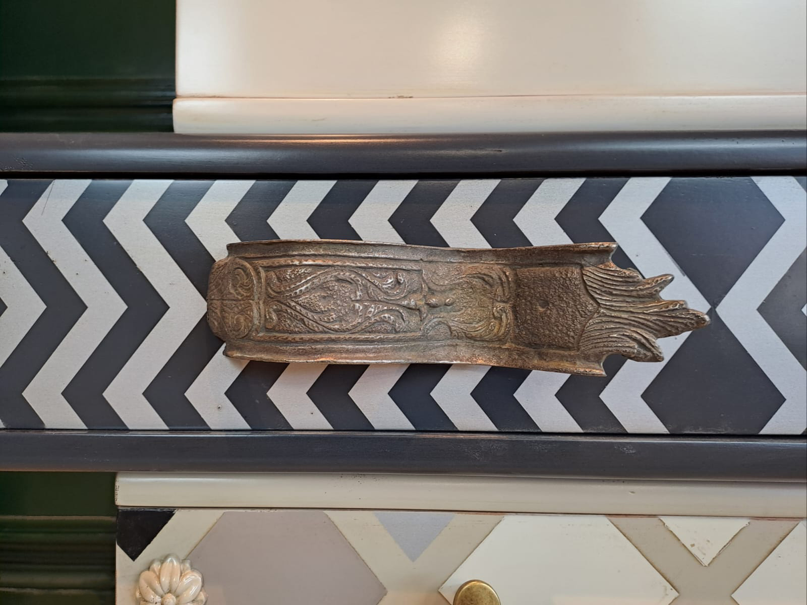 Detalle del tirador metálico del Sinfonier Alice sobre cajón con patrón chevron en tonos oscuros.