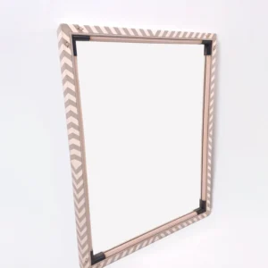 Vista en ángulo del Espejo Compás mostrando el marco geométrico en zigzag beige y topo.